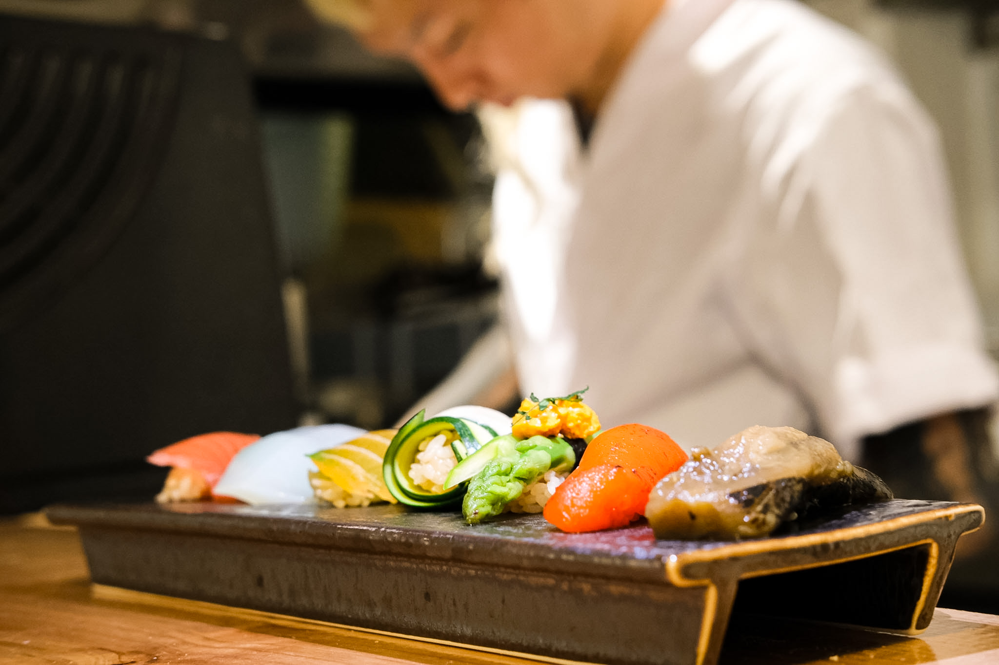 A lineup of nigiri with the chef preparing dishes in the background